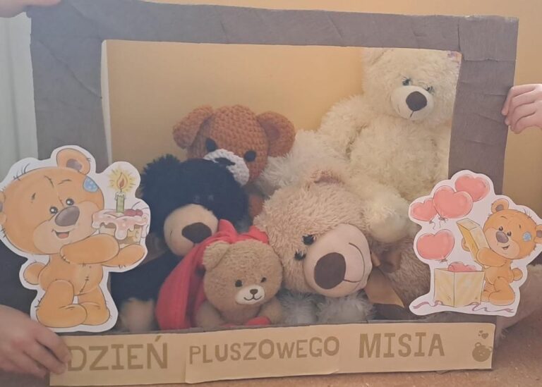 Grupa pluszowych misiów ustawiona w kartonowej ramce ozdobionej napisami ‘Dzień Pluszowego Misia’ oraz rysunkami uśmiechniętych misiów z tortem i balonami.