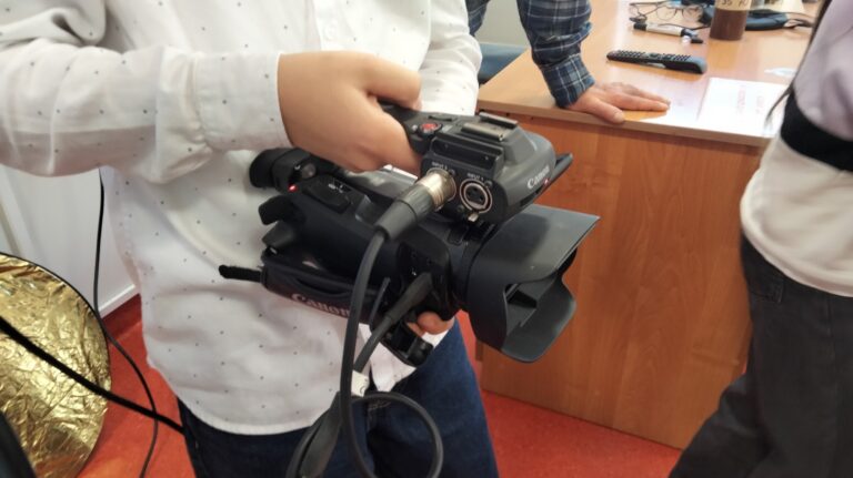 Uczeń trzyma w dłoniach profesjonalną kamerę wideo Canon podczas zajęć filmowych prowadzonych w klasie.