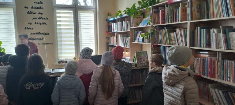 Uczniowie rozglądają się w bibliotece, wokół regały z książkami