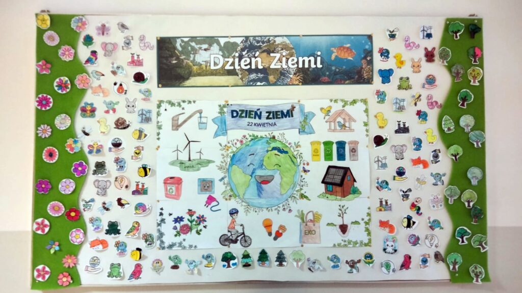 Tablica ścienna z napisem „Dzień Ziemi”. W centrum znajduje się plakat z uśmiechniętą planetą oraz ekologicznymi symbolami, takimi jak wiatraki, kosze do segregacji, rower, żarówki...