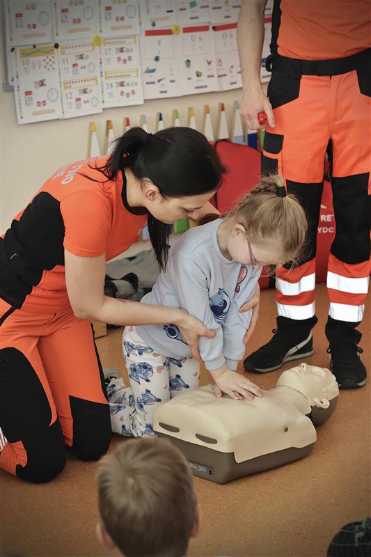 Ratowniczka medyczna uczy dziecko resuscytacji krążeniowo-oddechowej na fantomie.